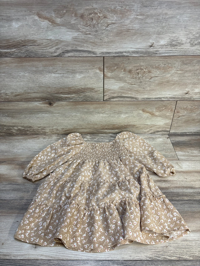 Tan floral baby dress with smocked bodice and long sleeves, laid on wood floor