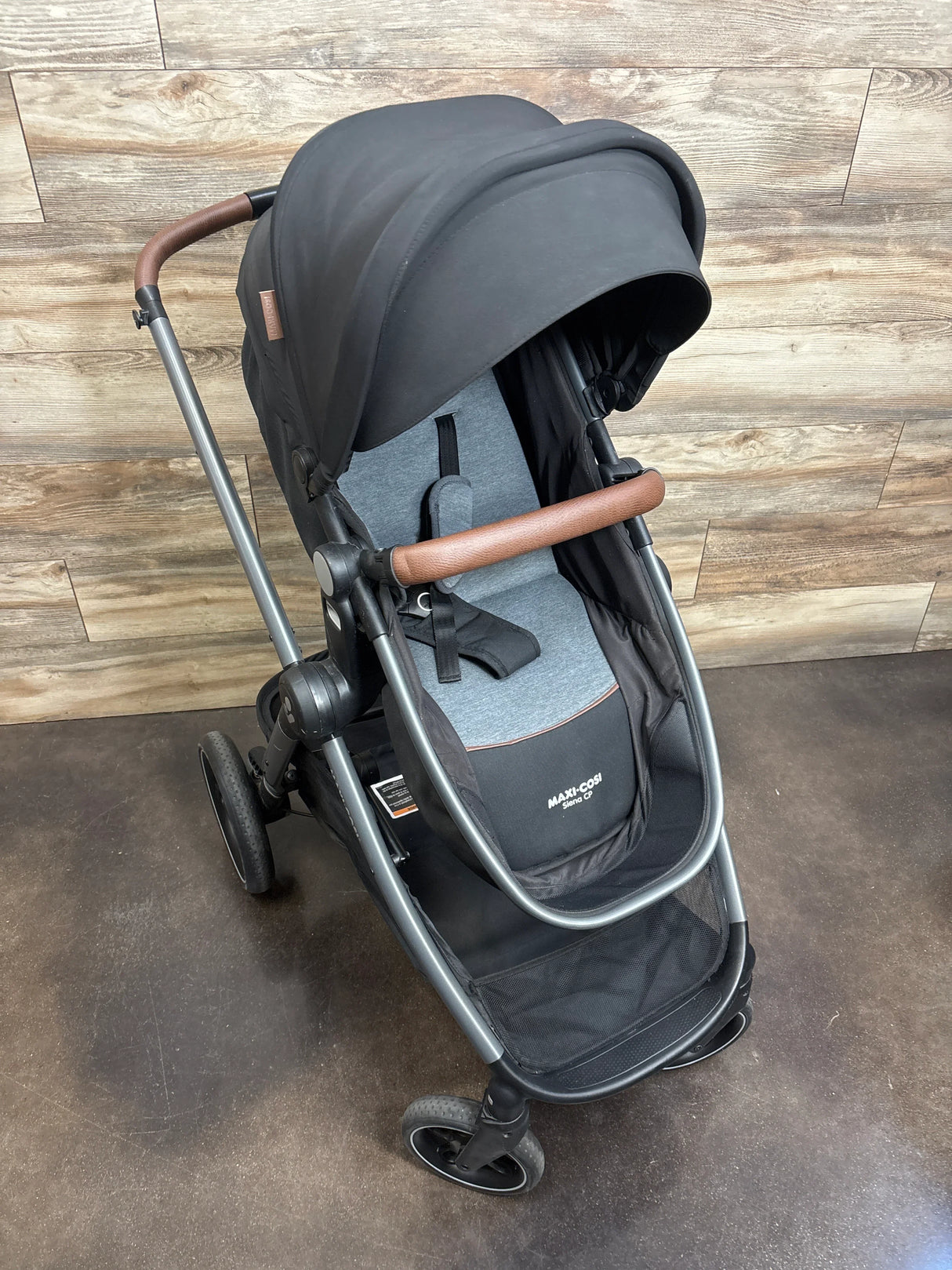Black and gray Maxi-Cosi baby stroller with brown handle, shown on wood background