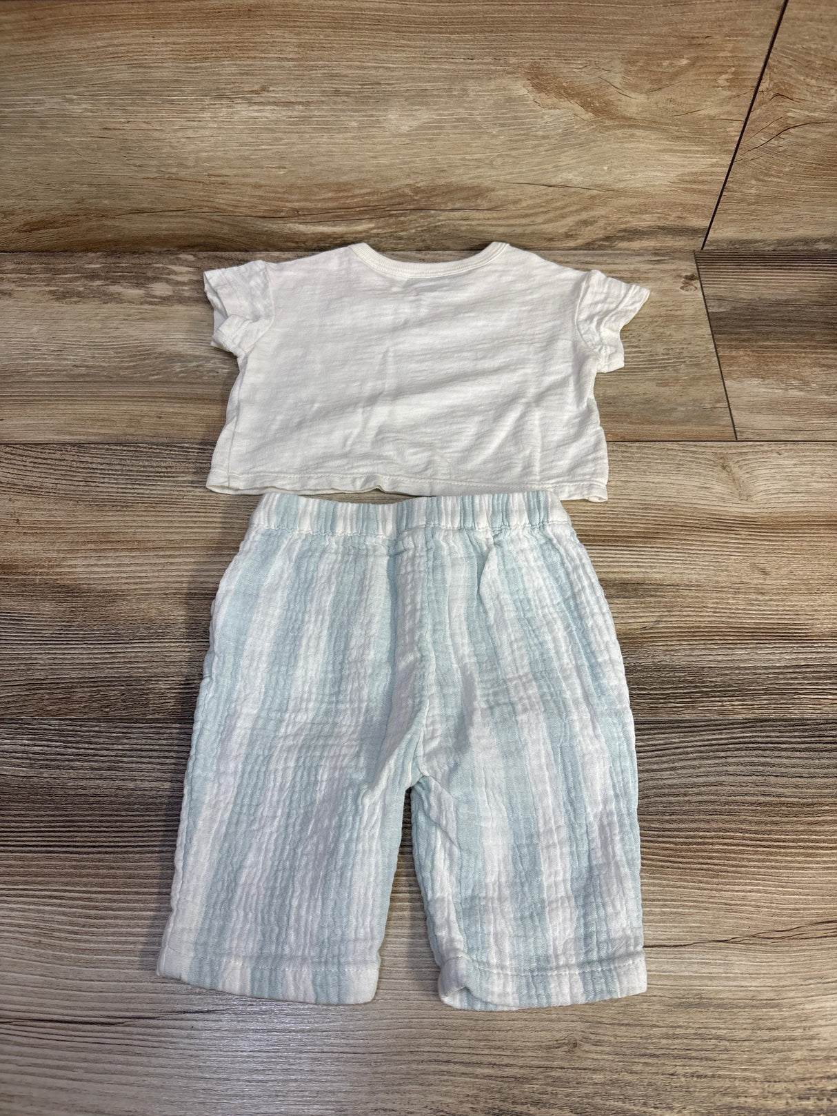 Flat lay of newborn white short-sleeve shirt and gauze light-blue striped pants showing gauze texture on wood floor