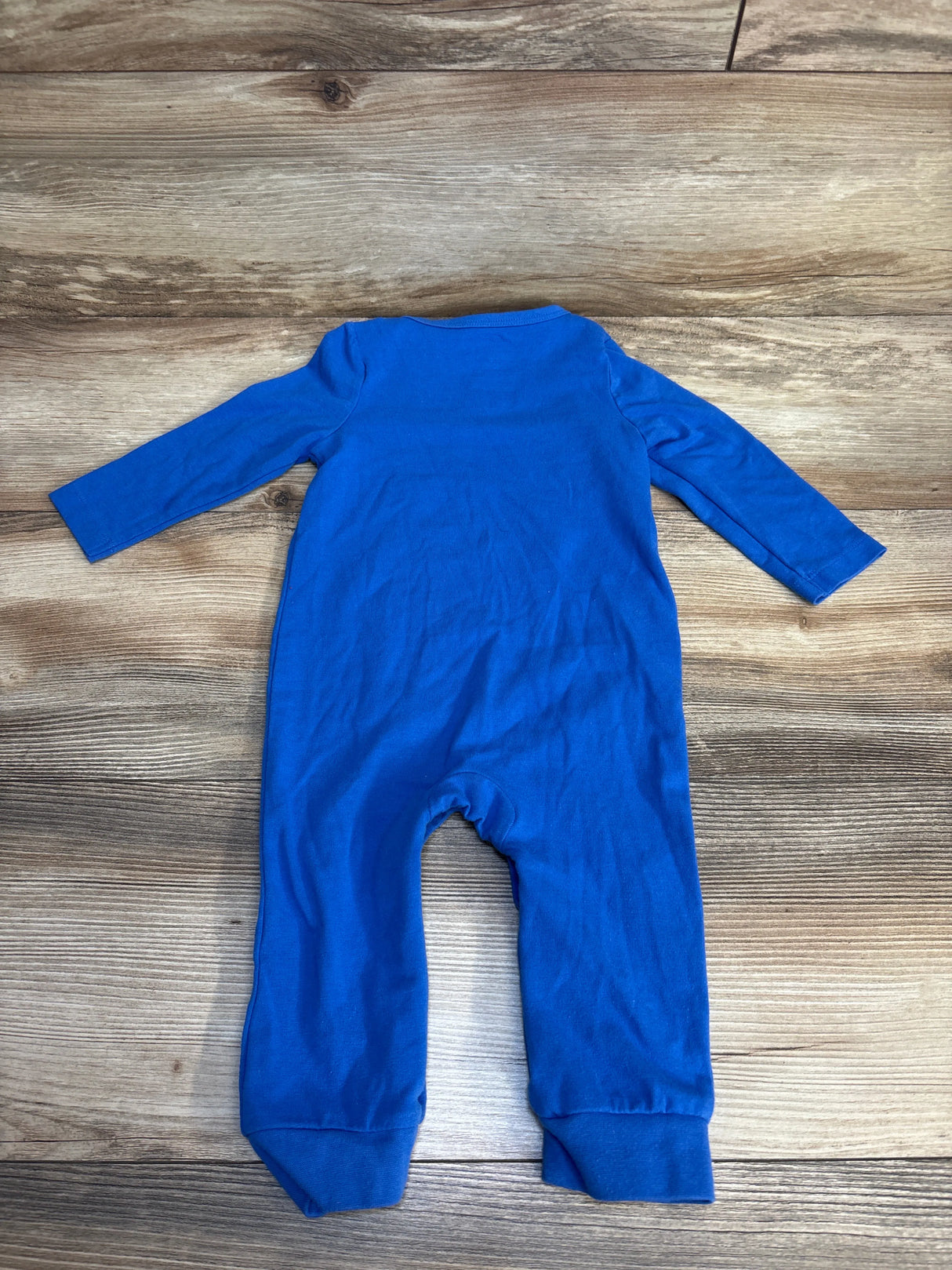 Blue baby onesie with long sleeves and legs, laid flat on wood floor