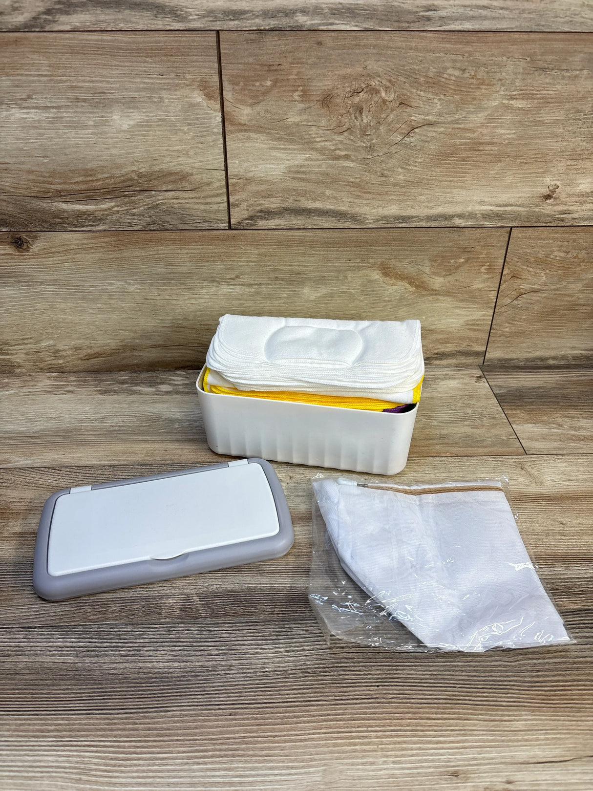 Front view of Famoplay baby wipe dispenser with 54 reusable white flannel wipes, gray lid, and mesh bag on wood background