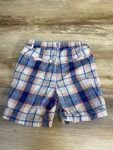 Plaid toddler boys shorts with blue, white, and peach check pattern on wood background
