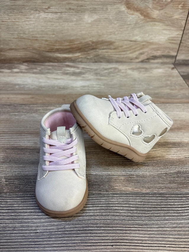 Light pink toddler shoes with heart cutout details and rubber soles on wood background