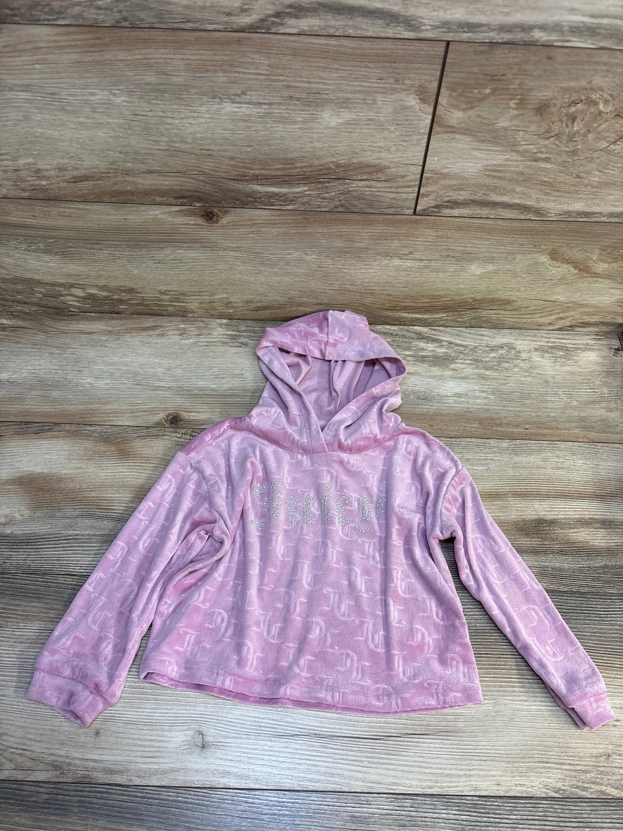 Pink Juicy Couture kids hoodie with logo print, laid on wood floor