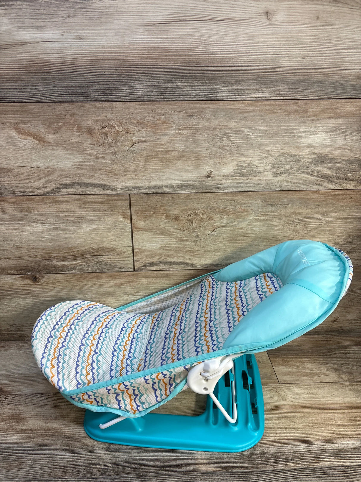 Side view of Summer Infant Foldaway baby bather showing turquoise base, padded head support, patterned seat on wood background