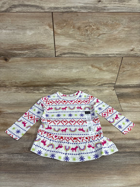 Flat lay of white peplum baby shirt with pink unicorns, rainbows, and fair-isle motifs, 9M tag on wood floor