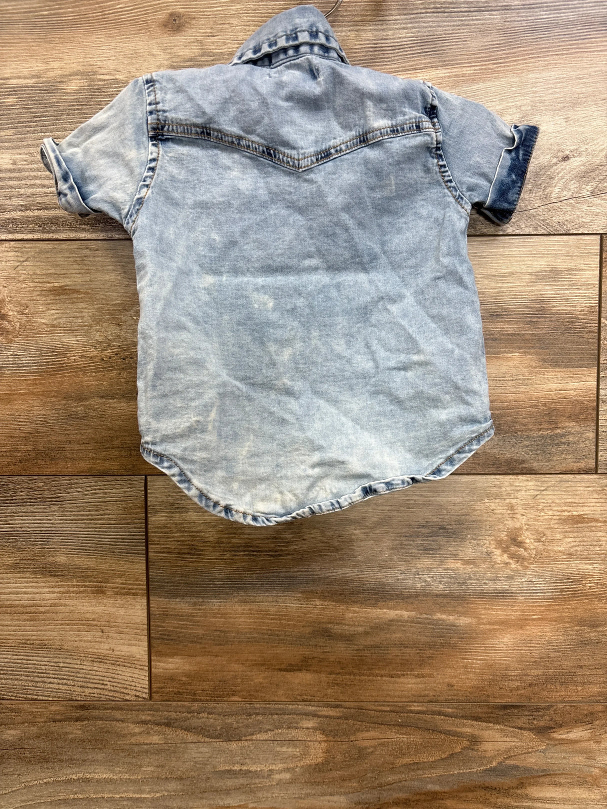 Back view of 7 For All Mankind denim button-down (12M) showing rolled sleeves and faded blue wash on wood floor