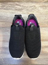 Black slip-on kids sneakers with white soles and pink insoles on wooden floor