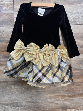 Front view of Iris & Ivy black velvet toddler dress showing long sleeves, three gold bows and gold-gray plaid skirt on wood floor