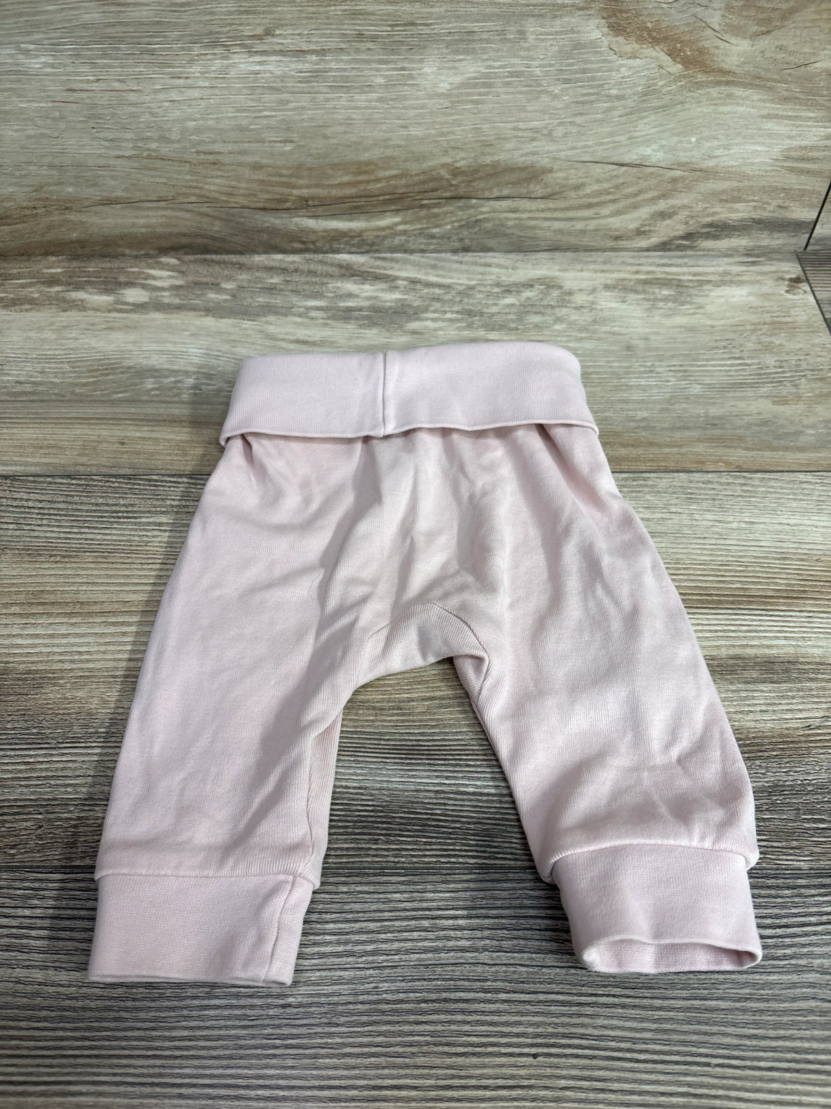 Flat lay of pink H&M foldover-waist baby pants showcasing foldover waistband and cuffed legs on light wood background