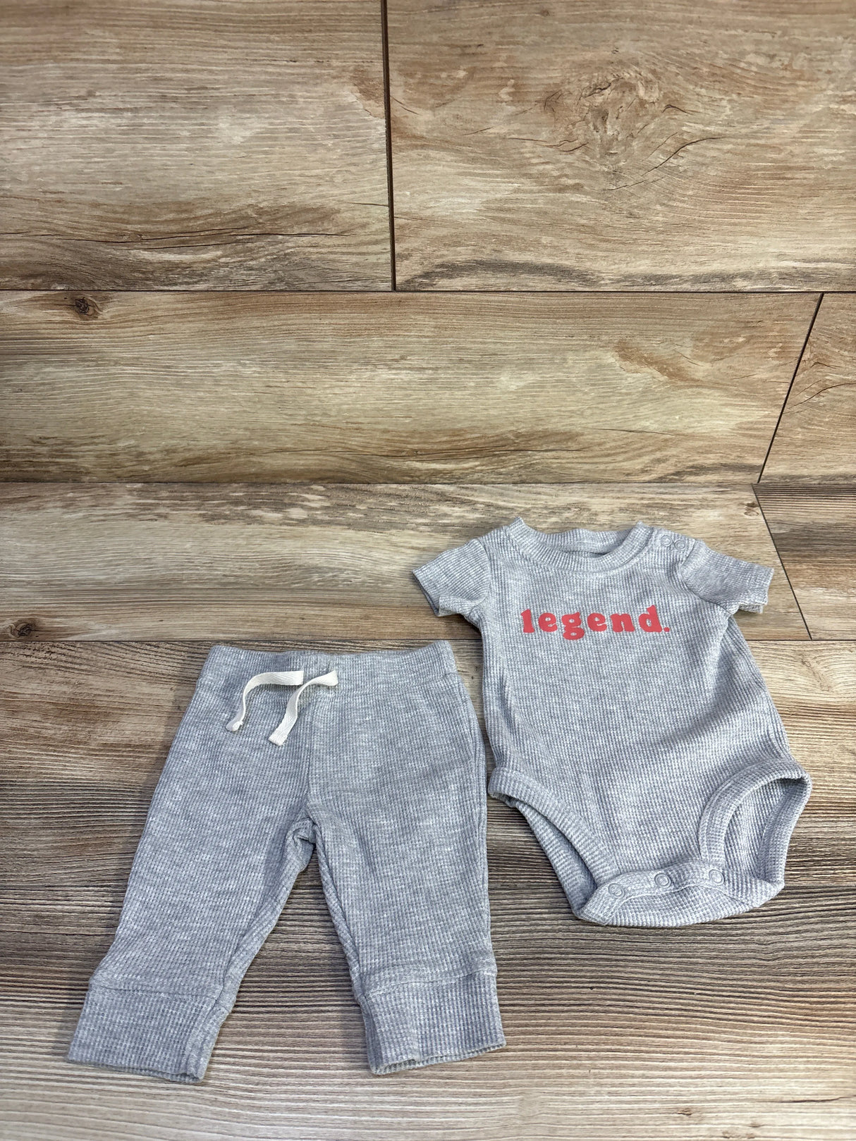 Flat lay of Carter's 2-piece gray waffle-knit bodysuit and pants (3M) showing red legend text and ribbed texture on wood