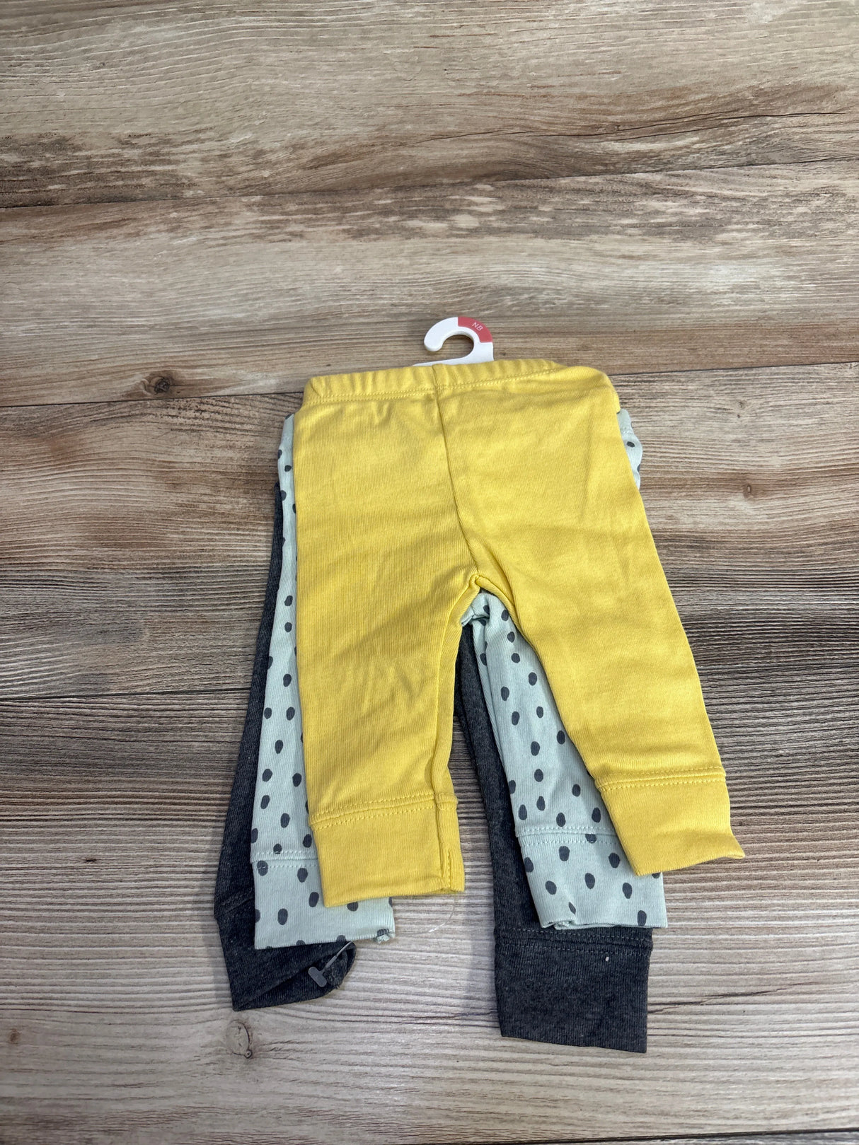 Three-pack of newborn baby leggings in yellow, white with black polka dots, and charcoal gray on wooden background