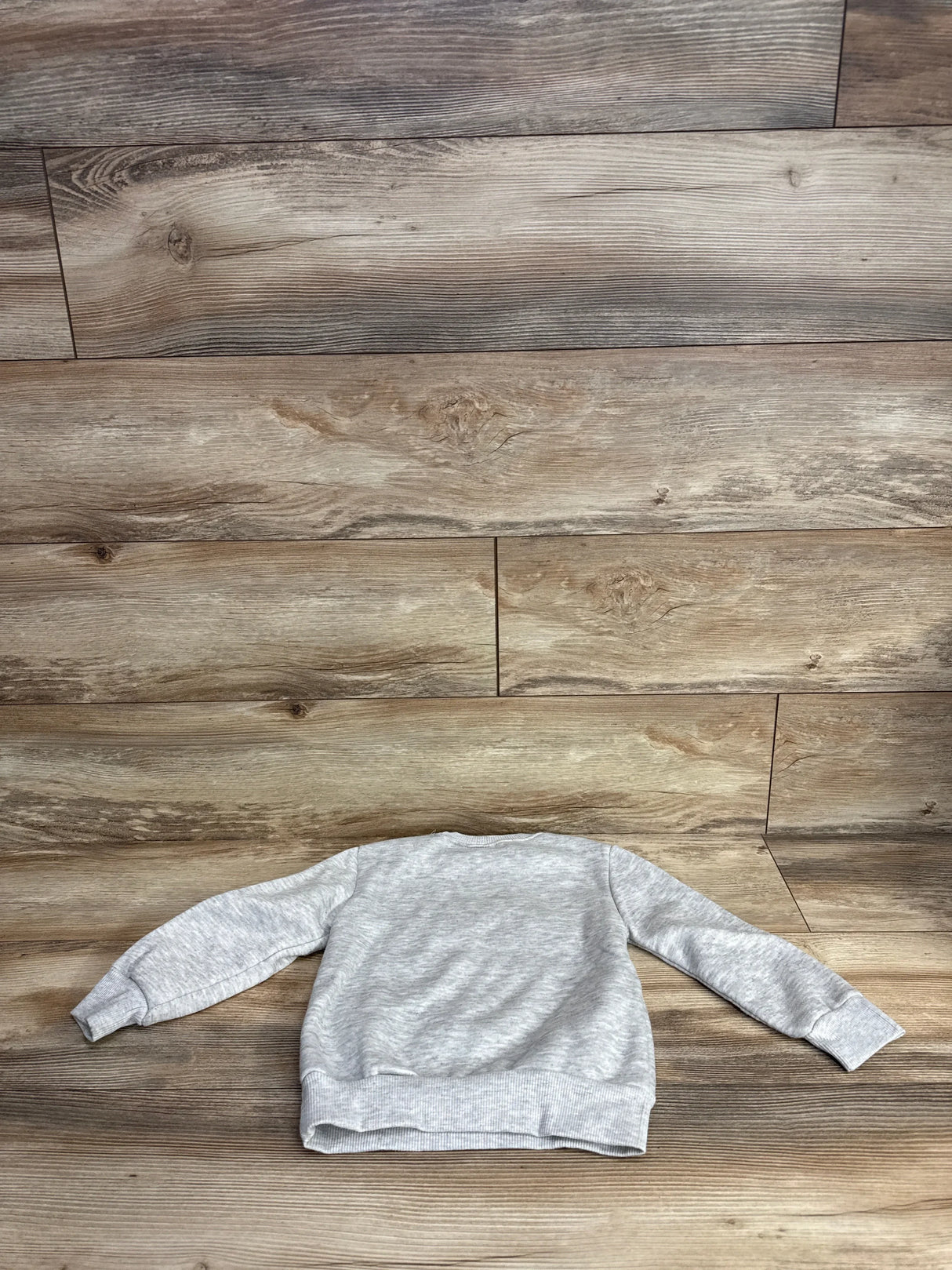 Light gray kids crewneck sweatshirt laid flat on wood floor background