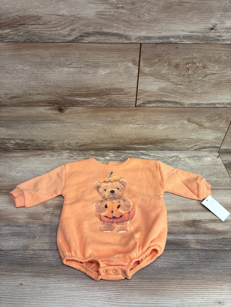 Front view of orange Grayson Mini Pumpkin Bear bubble romper with long sleeves and snap closures on wood planks