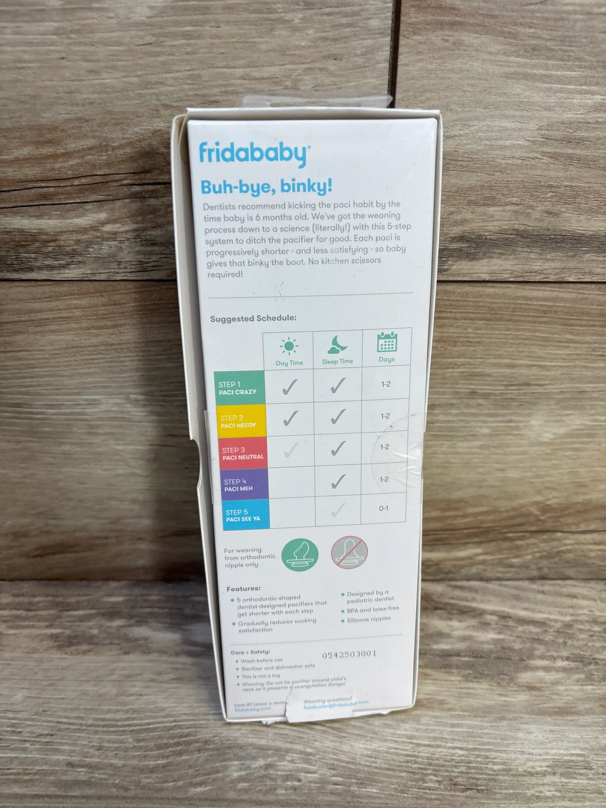Back view of FridaBaby Pacifier Weaning System box showing 5-step weaning schedule and product features on wooden surface