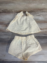 Yellow and white striped baby outfit with ruffled top and shorts, laid on wood floor
