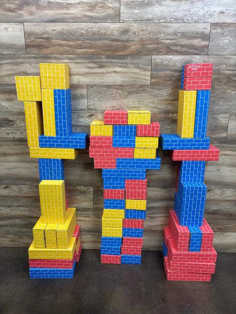 Front view of Bankers Box Heavy Duty Jumbo Cardboard Building Blocks 74ct arranged as red, blue, and yellow towers on dark wood