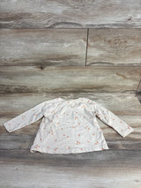 White long-sleeve toddler shirt with small orange fruit pattern laid flat on wooden floor