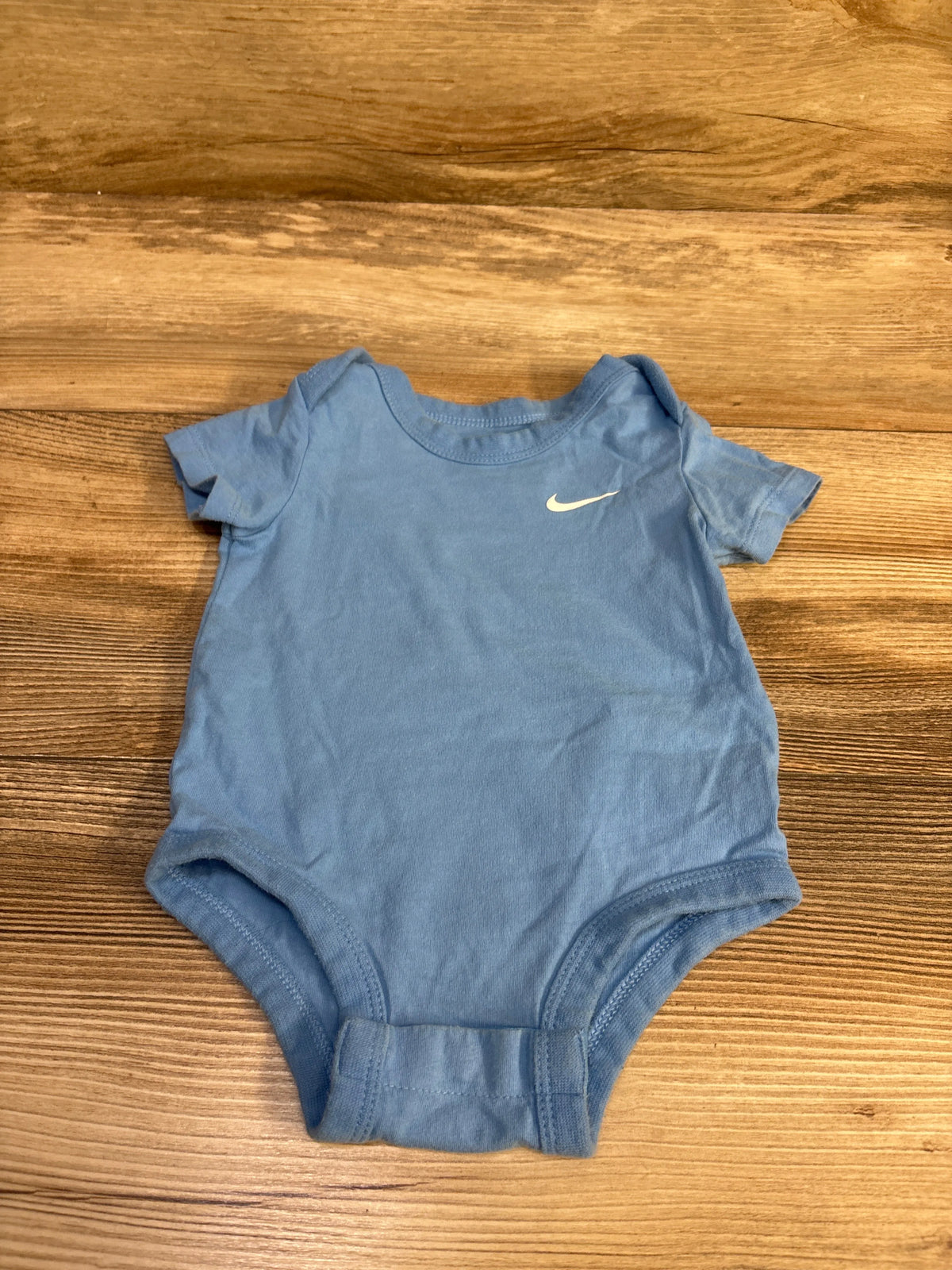 Light blue Nike baby bodysuit for 6 month old on a wooden surface