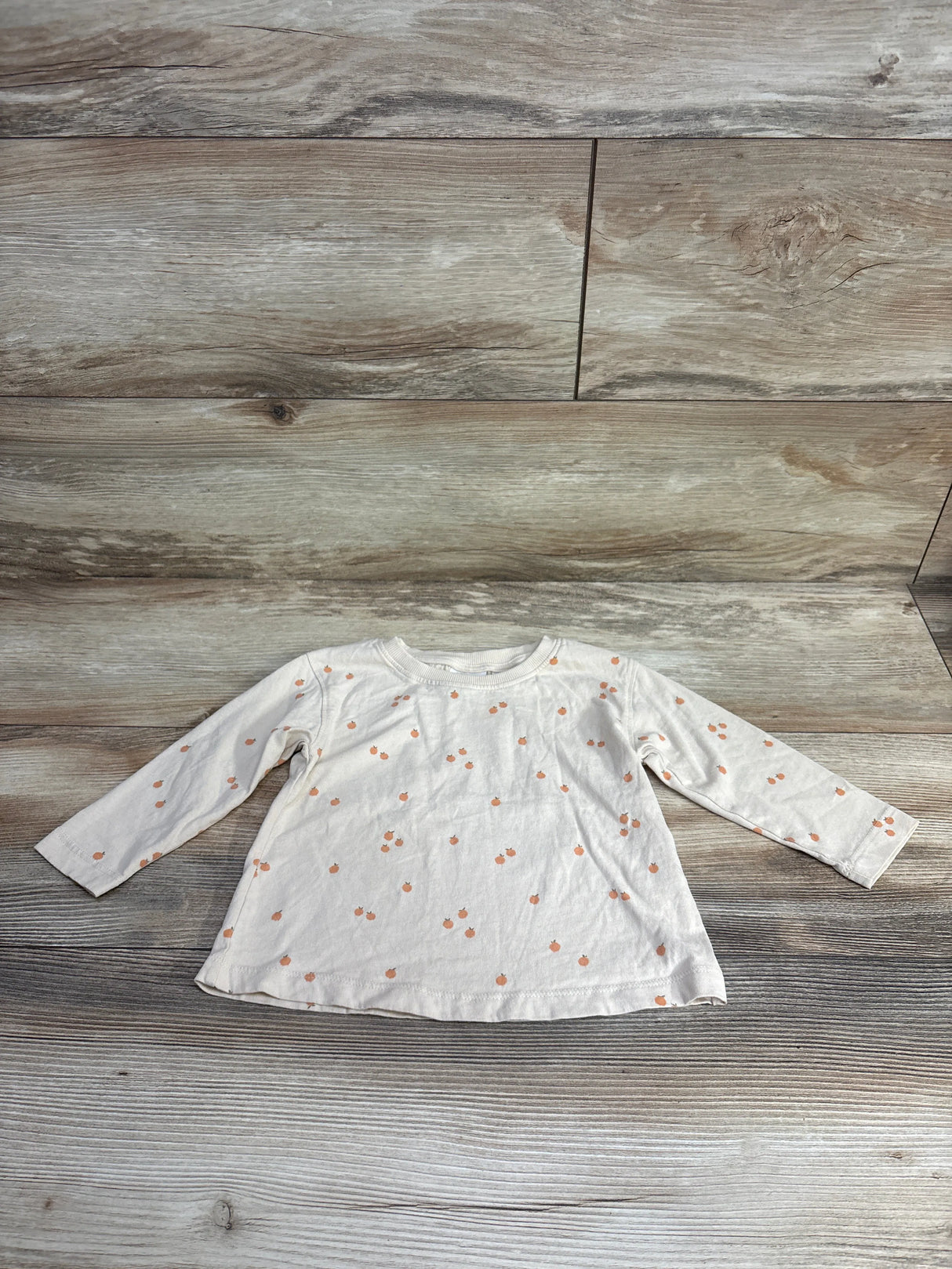 White long-sleeve toddler shirt with small orange pumpkin print on wooden background