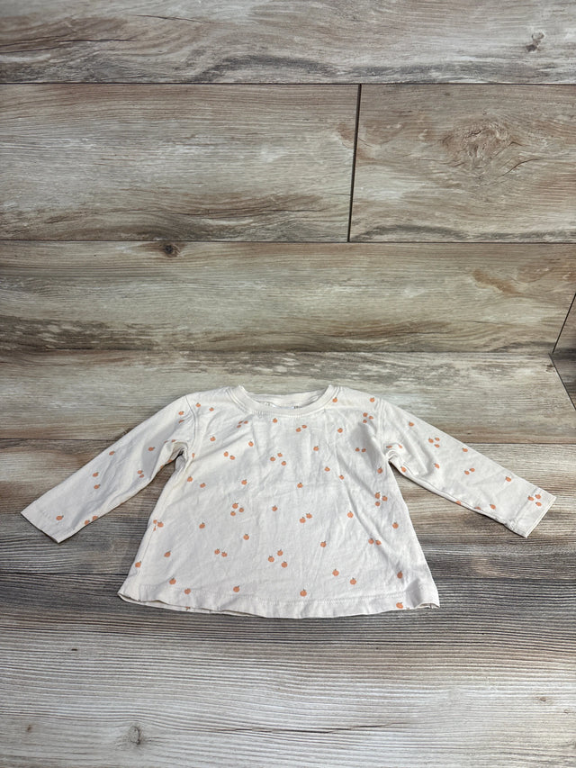 White long-sleeve toddler shirt with small orange pumpkin print on wooden background