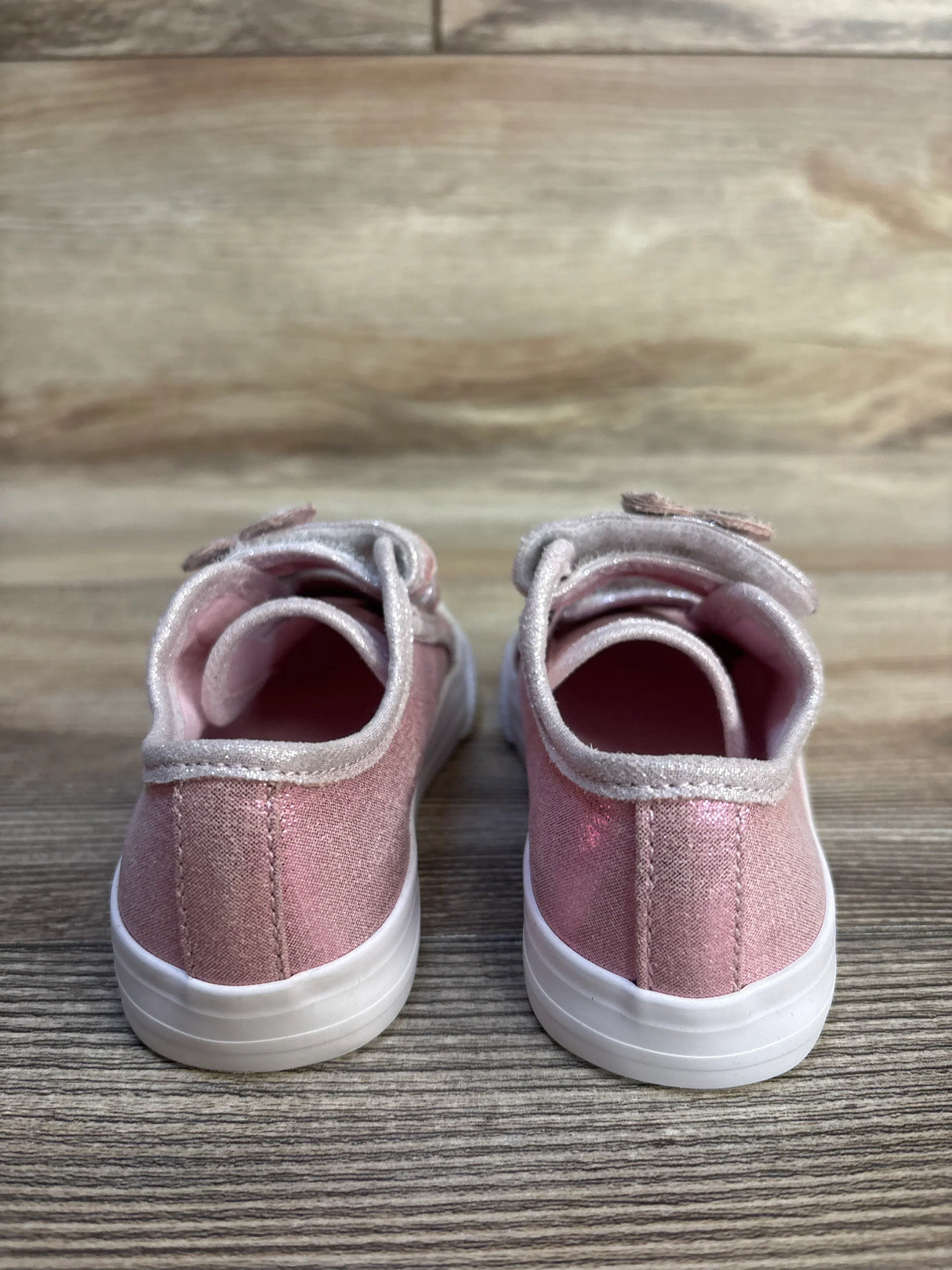 Pink glitter toddler sneakers with white soles on wood floor, rear view