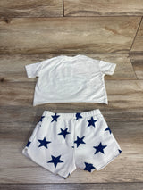 Flat lay of Grayson Mini 2-piece USA shirt and shorts showing back of ivory tee and white shorts with navy stars on wood