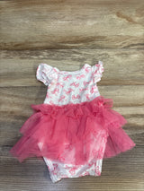 Flat lay of white baby bodysuit dress with pink bow print showcasing ruffled cap sleeves and layered pink tulle tutu on wood background