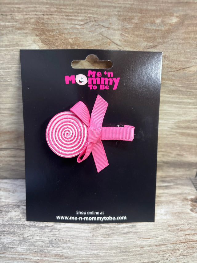 Front view of pink lollipop-shaped toddler hair bow showcasing spiral ribbon design and clip on black Me n Mommy To Be display card with wooden background