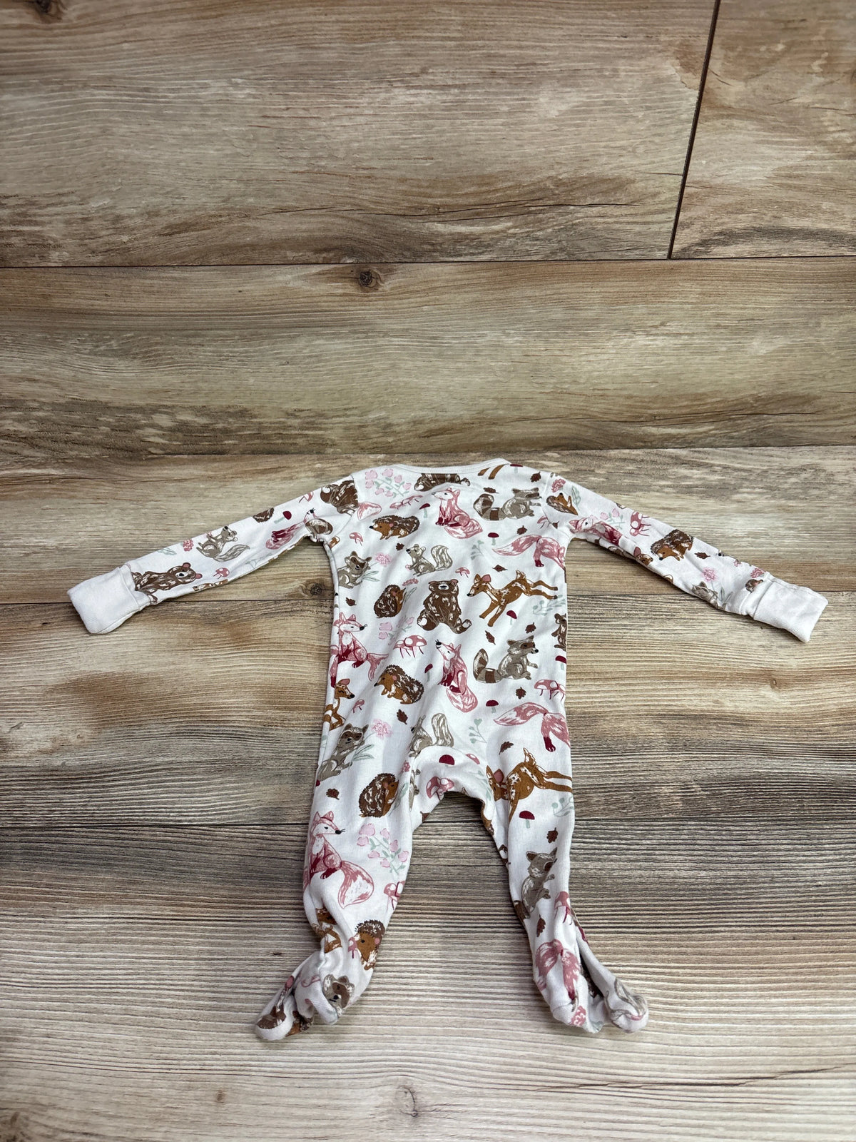 Top-down view of Member’s Mark ivory footed sleeper in size 3 months showcasing woodland animal print on a wood-look background