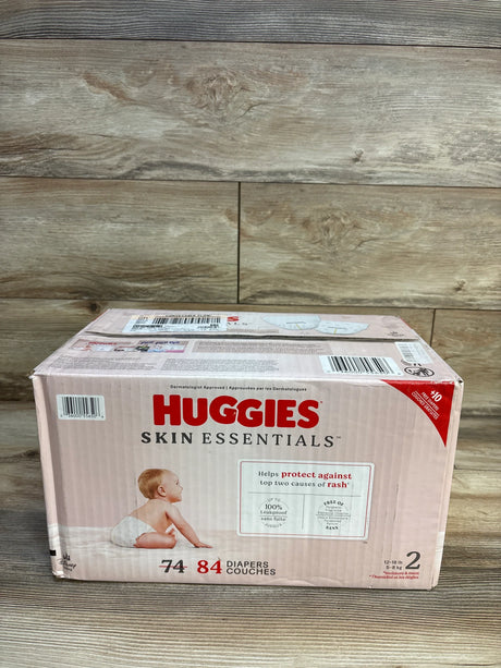 Huggies Skin Essentials size 2 baby diapers box, 84 count, for 12-18 lb infants on wood floor