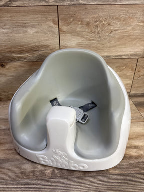 Three-quarter view of Bumbo Multi Seat showing grey inner seat, white base with embossed logo and harness on wood floor