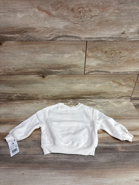 Back view of Grayson Mini Pumpkin Bear sweatshirt in ivory showing long sleeves and ribbed trim on a wood background