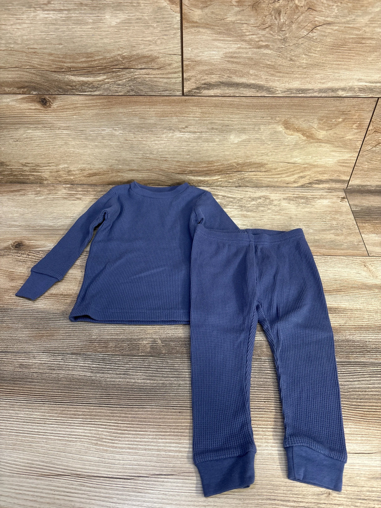 Flat lay of blue 2-piece waffle knit baby pajama set size 12 months showing long-sleeve crew top and cuffed pants on wood background
