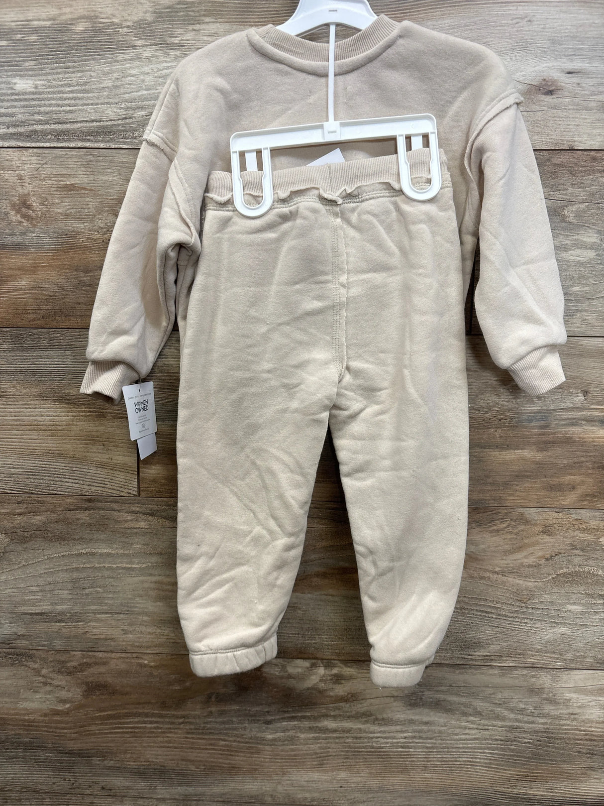Front view of beige Grayson Mini 2-piece fleece crewneck and joggers with elastic waistband, ribbed cuffs on hanger against wood background