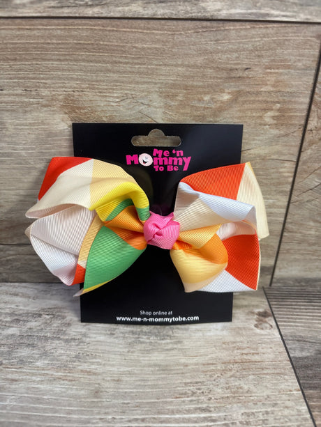 Front view of a large multicolor hair bow showcasing layered ribbon loops on a black display card over a wood surface