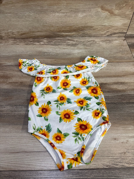 Flat lay of white baby off-shoulder romper showcasing ruffled neckline and yellow sunflower print on wood background