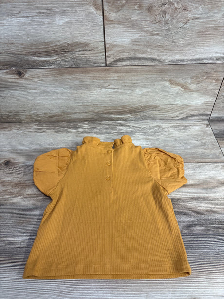 Mustard yellow toddler top with puff sleeves and three back buttons on wood background