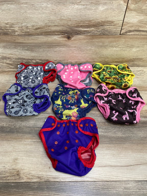 Overhead view of seven Best Bottom diaper covers in mixed prints, showing snaps and elastic leg openings on wood floor