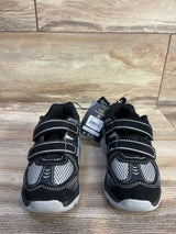 Front view of toddler two strap black sneakers showing Velcro straps, gray mesh and white soles on wood background
