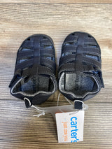 Top view of Just One You Harrison baby fisherman sandals, navy, showing closed-toe woven straps and Carter's tag on wood floor