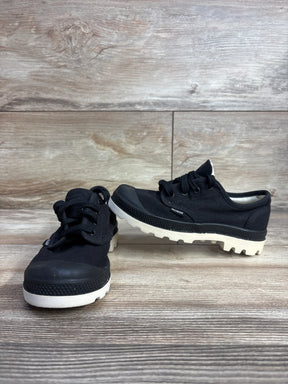 Pair of black Palladium kids canvas sneakers with white rugged soles on wooden floor