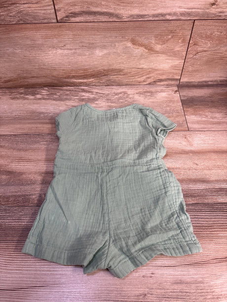 Flat lay of Baby Gap muslin shortie romper showcasing sage green crinkled fabric and gathered waist on wood background