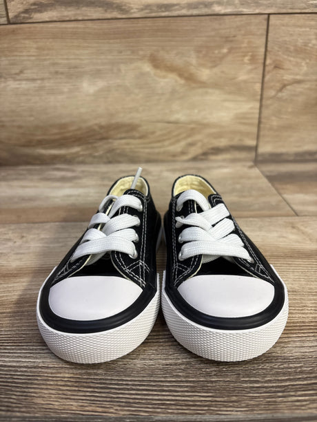 Front view of black toddler low-top sneakers size 5C showcasing white rubber toe caps, thick white soles, and white laces on wood floor