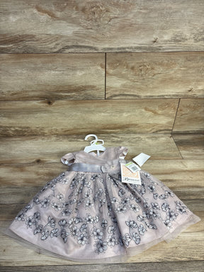 Pink floral embroidered baby dress with short sleeves and satin waistband on wood background