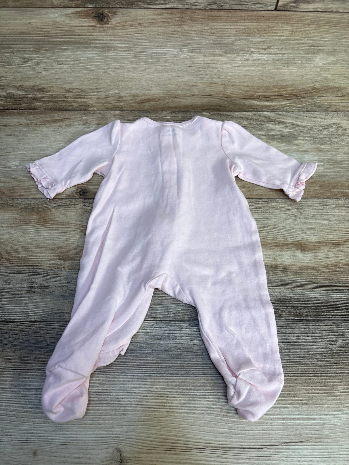 Pink baby footed onesie with ruffled sleeves, soft newborn sleepwear on wood floor