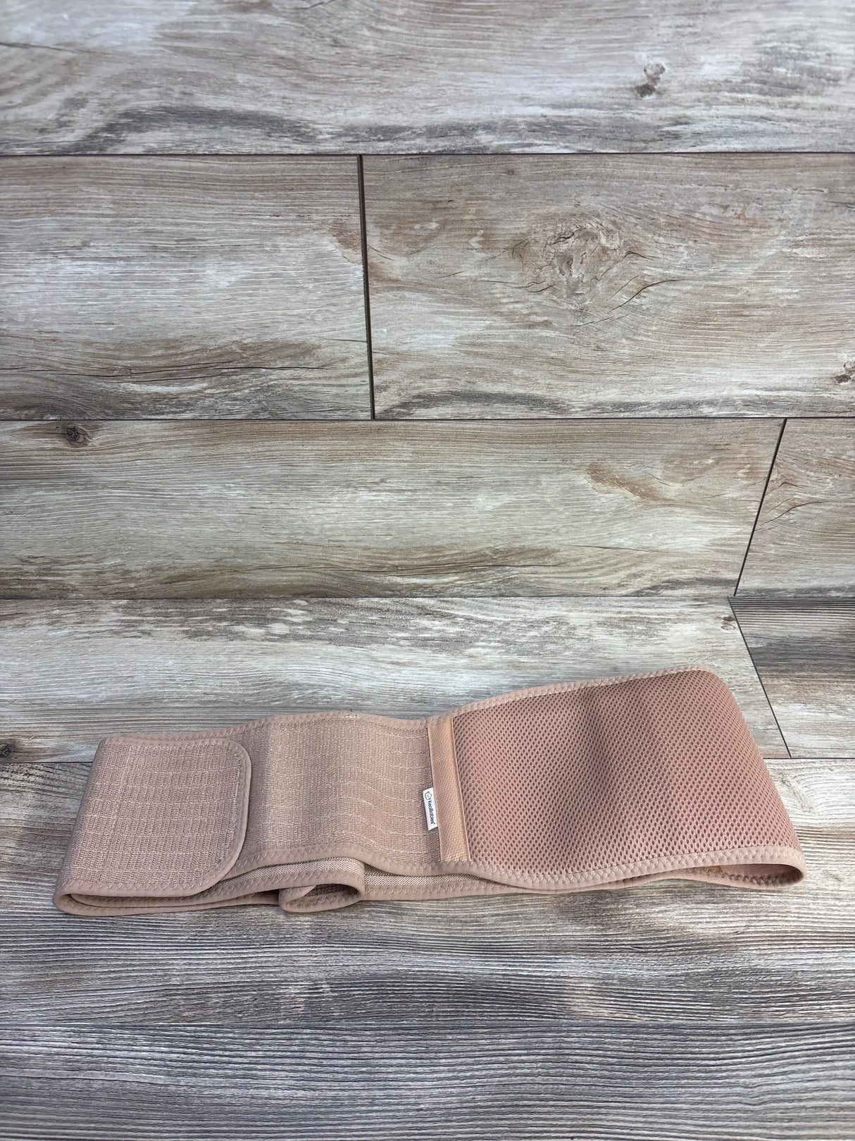 Flat lay KeaBabies Ease maternity support belt, beige, with breathable mesh panel and Velcro closure on wood background