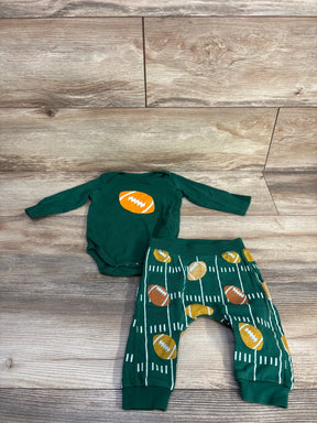 Flat lay of green 2-piece football baby outfit with orange football chest graphic and matching printed pants on wood backdrop