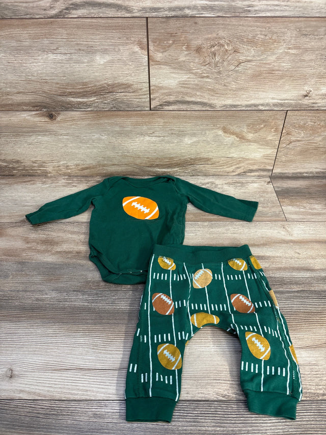 Flat lay of green 2-piece football baby outfit with orange football chest graphic and matching printed pants on wood backdrop