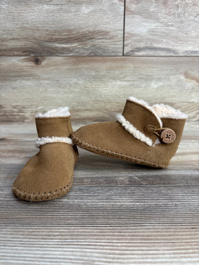 Pair of tan suede baby UGG boots with white fleece lining and button detail on wood surface